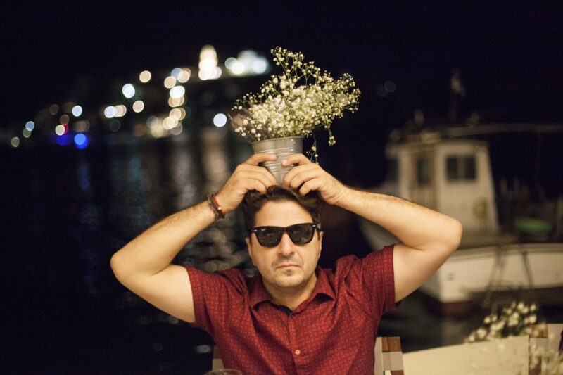 Guest puts foe fun small vase with flowers on his head. Photography Ioanna Chatzidiakou