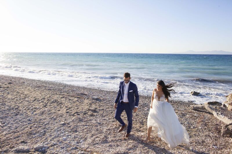 Bride and Groom walking away from the sea. Photography Ioanna Chatzidiakou