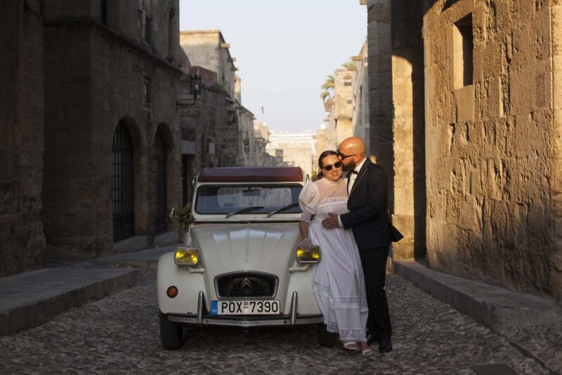 Η νύφη και ο γαμπρός μετά το γαμο τους στην οδο Ιπποτών στη παλιά πόλη της Ρόδου με ένα vintage αμαξι